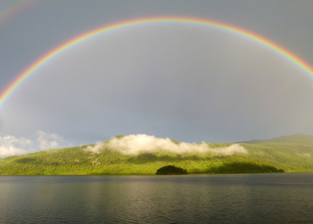 A rainbow, over an island. The rainbow symbolizes the overarching trends of humankind. The island reflects primordial humankind. The cloud, blue sky, and ocean reflect peace of mind.